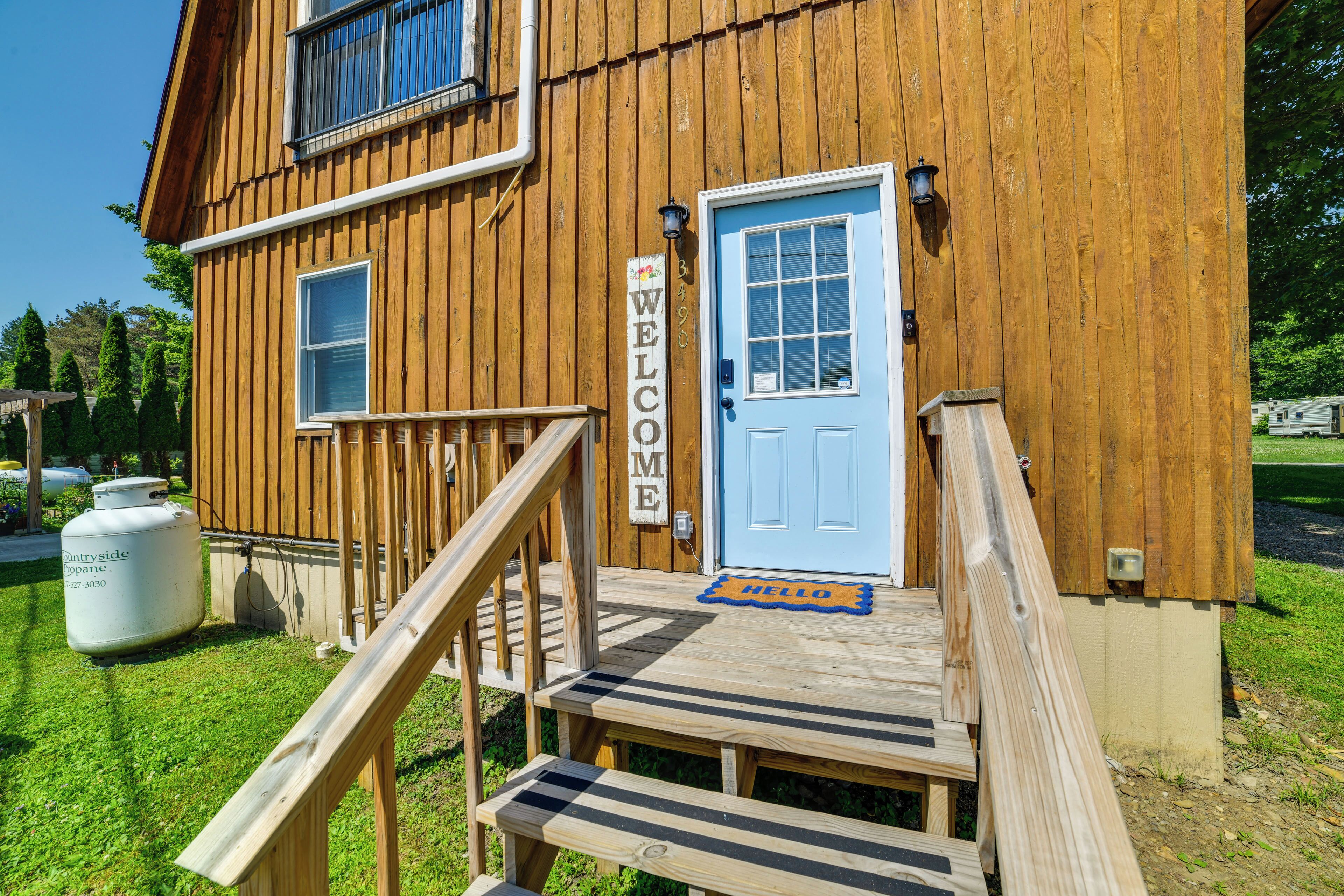 Un bâtiment en bois avec une porte bleue, une pancarte indiquant « BIENVENUE » et un paillasson sur lequel est écrit « BONJOUR ».