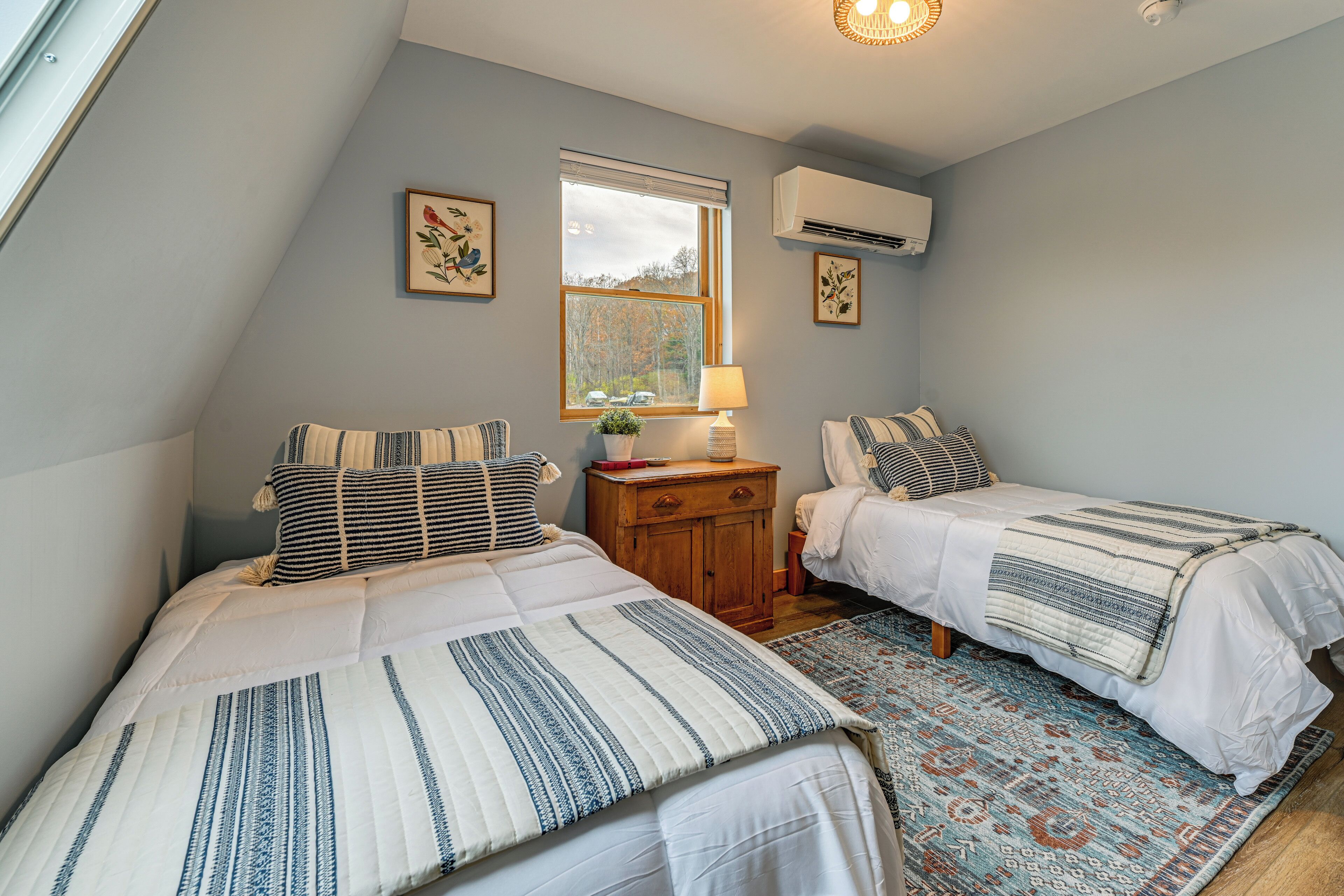 A bedroom with two beds, a window, an air conditioner, and a rug.