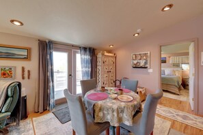 Ein Essbereich mit einem Tisch für vier Personen, Stühlen, einem Fenster mit Vorhängen, einem Heizkörper und Blick in ein Schlafzimmer.