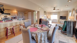Un vaste espace de vie comprenant une salle à manger avec une table pour quatre personnes, une cuisine dotée de meubles en bois et un coin salon confortable avec un fauteuil à bascule.