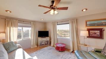 Una habitación con ventilador de techo, televisor, una mesa roja, sofá y vistas al exterior.