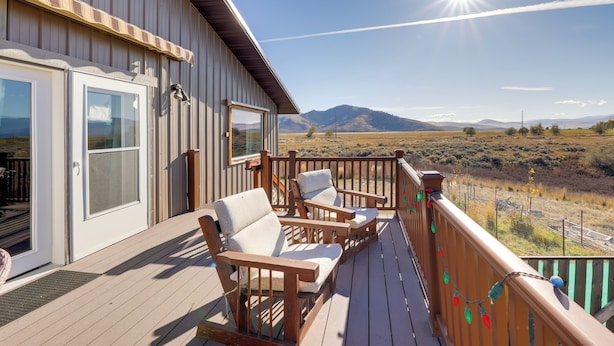 Une terrasse en bois avec deux chaises et une table, offrant une vue sur un paysage montagneux.