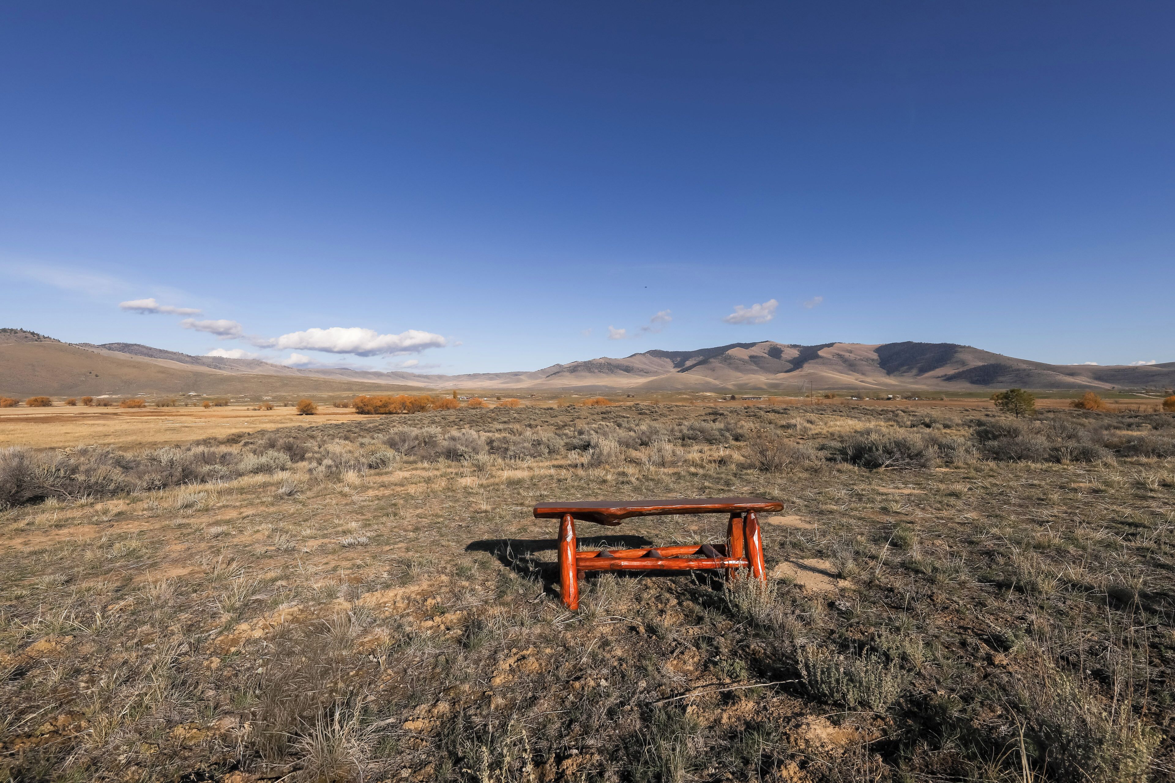 A wooden bench in a dry, grassy field with mountains in the background.
