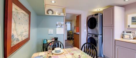 Uma sala de jantar com mesa posta para dois, cozinha equipada e corredor que dá para outro quarto.