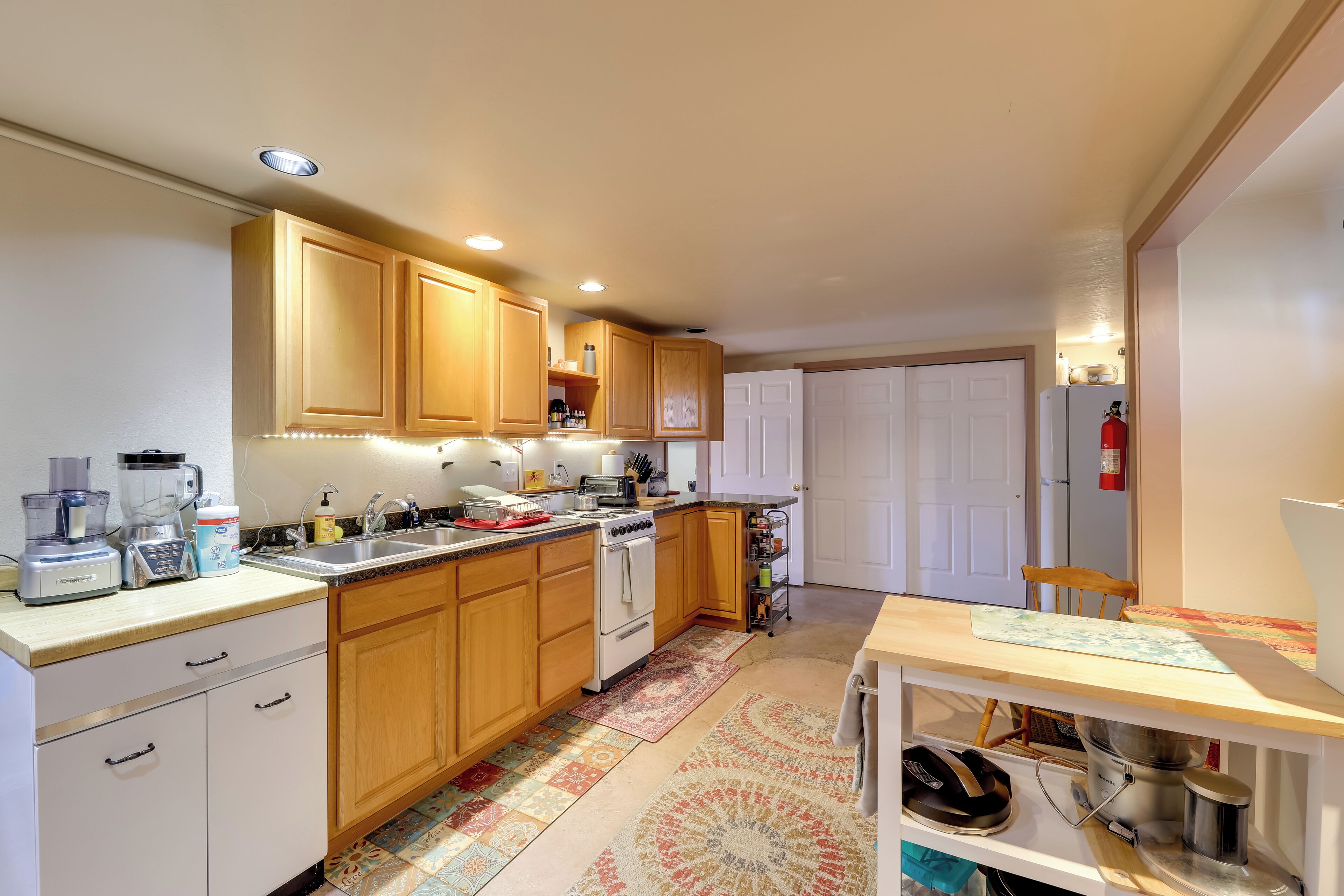 A compact kitchen with wooden cabinets, a built-in oven, a sink, and a small dining area with a table.