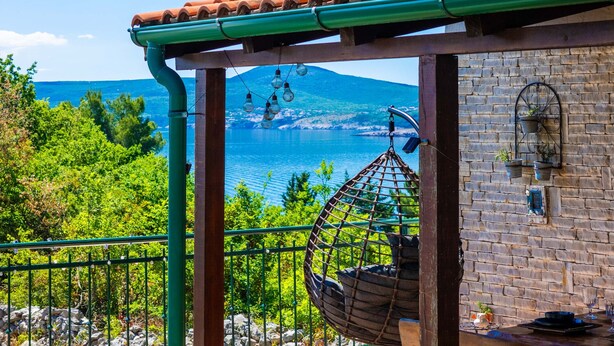 A balcony with a hanging chair, a brick wall, and a view of a lake and mountains. - Villa Ruby beachfront by Villas Guide (Dobrinj)