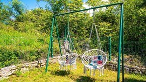 A swing set with two swings, surrounded by greenery and a stone wall. - Villa Ruby beachfront by Villas Guide (Dobrinj)