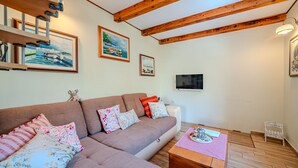 A living room with a sofa, pillows, a flat-screen TV, wooden beams, and artwork on the walls. - Villa Ruby beachfront by Villas Guide (Dobrinj)