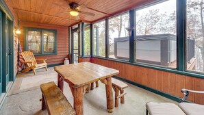 Une terrasse en bois avec une table et des bancs, de grandes fenêtres et un ventilateur de plafond.