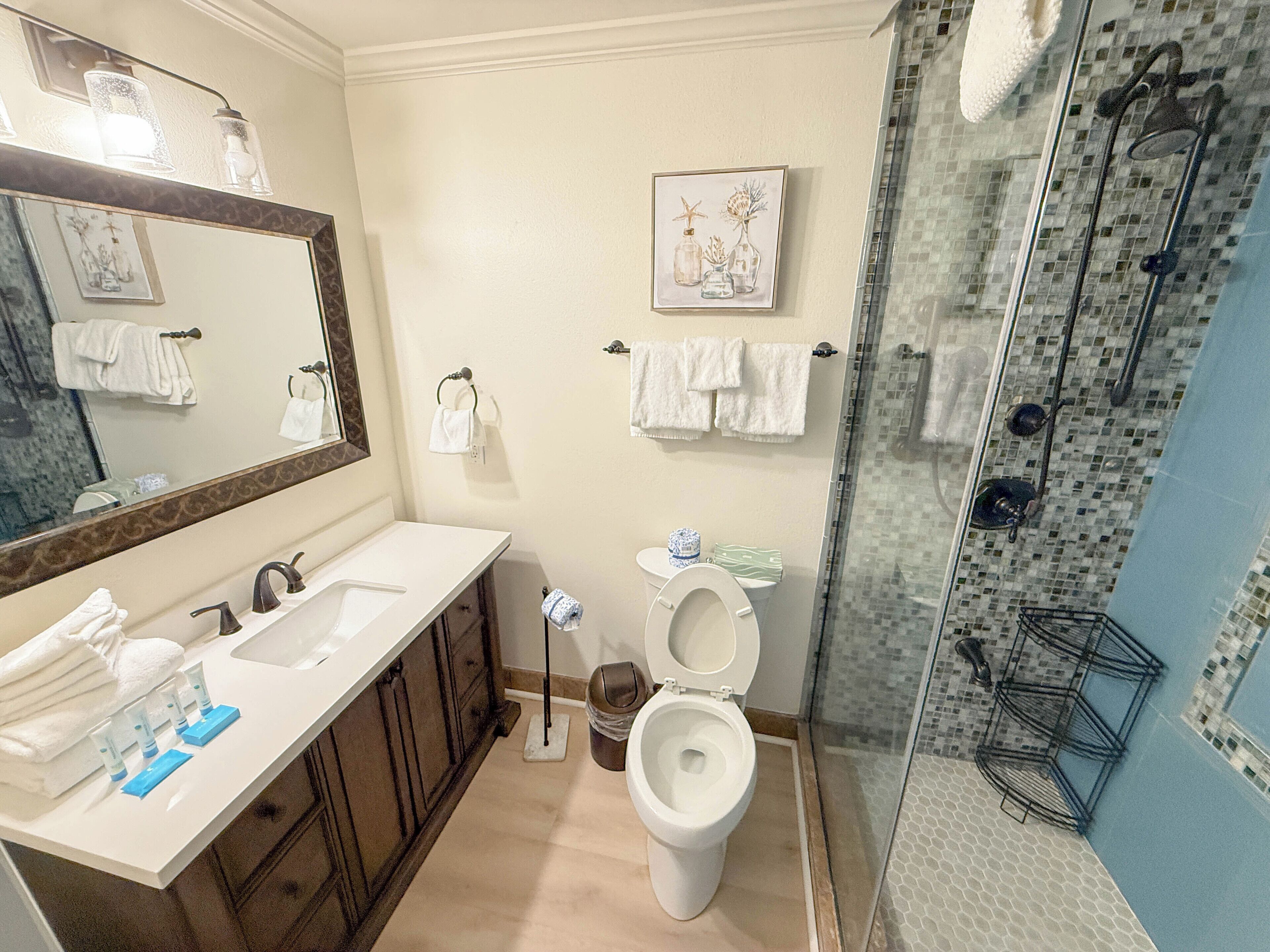 A bathroom with a large mirror, two sinks, a toilet, and a glass-enclosed shower area.