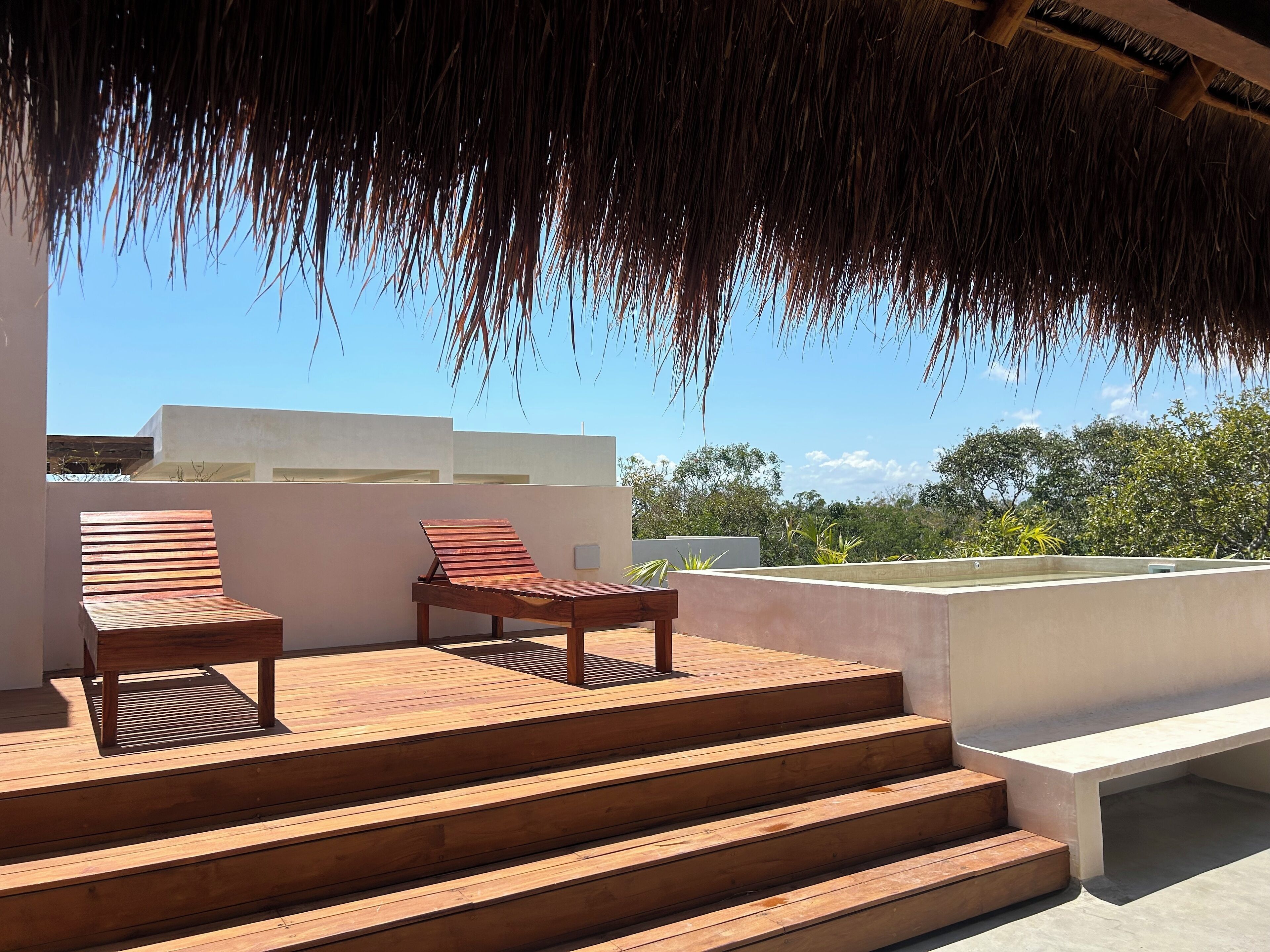 A wooden deck with steps leading to a seating area with two lounge chairs.