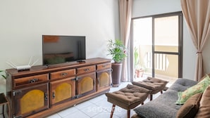 Una sala de estar con televisor sobre un mueble de madera, un sofá y una planta en maceta.