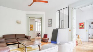 A modern living room with a brown sofa, white armchairs, a wooden coffee table, and a ceiling fan. - IMMERSE YOURSELF IN THE AUTHENTIC PARISIAN LIFESTYLE AT BLVD SAINT GERMAIN (Paris)