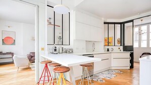 A modern kitchen with white cabinets, a central island with stools, and a large mirror. - IMMERSE YOURSELF IN THE AUTHENTIC PARISIAN LIFESTYLE AT BLVD SAINT GERMAIN (Paris)