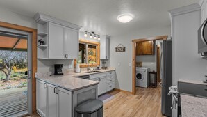 A modern kitchen with grey cabinets, a stainless steel refrigerator, a built-in oven, and a window overlooking a garden.