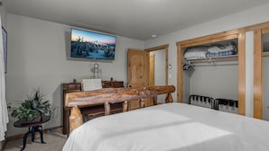 A bedroom with a bed, a wooden bench, a television, a piano, and a closet with shelves.