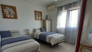 Un dormitorio con dos camas, ventilador de techo, armario y ventana con cortinas.