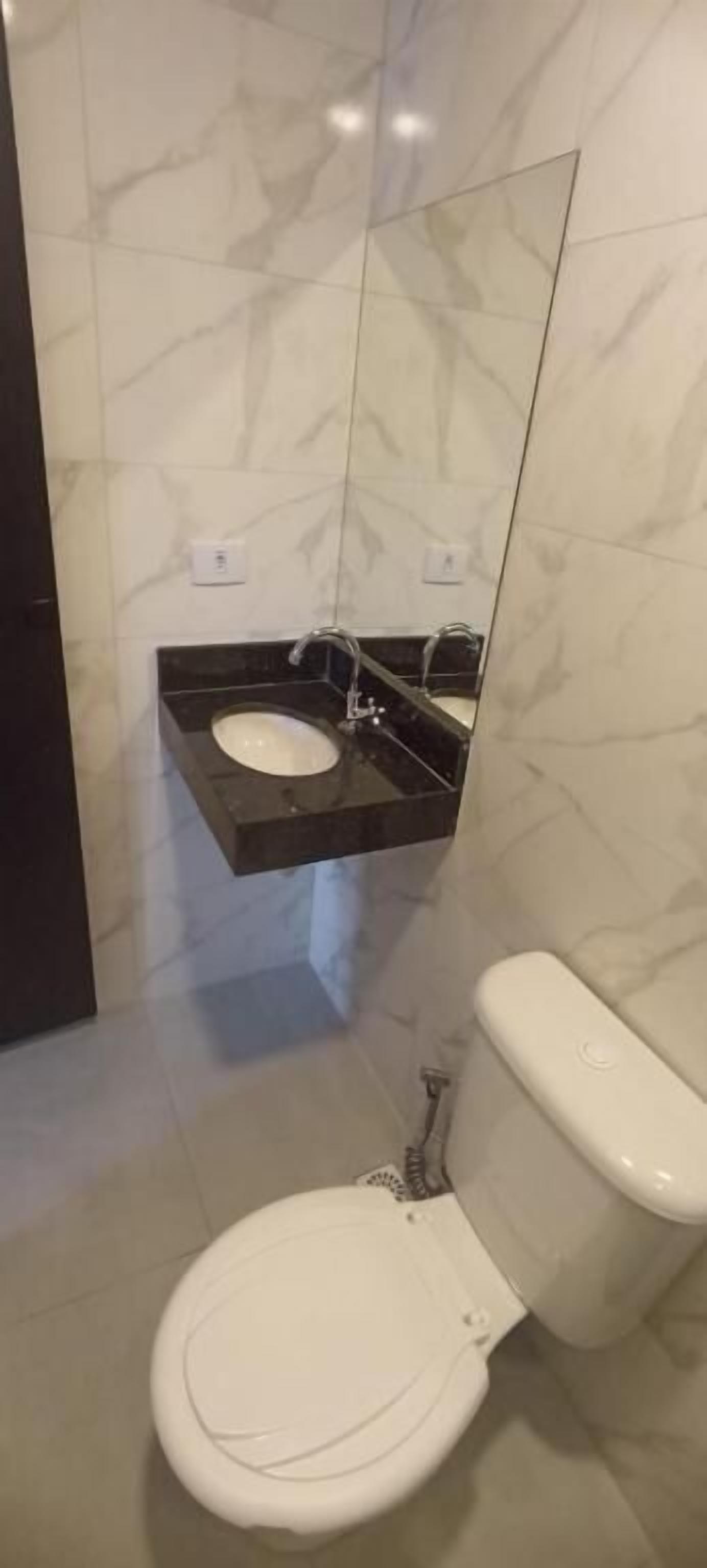 Un baño con inodoro blanco, lavamanos negro y un espejo sobre el lavamanos.