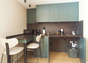 Una kitchenette compacta con microondas, cafetera y pileta. Hay dos sillas y un pequeño basurero.