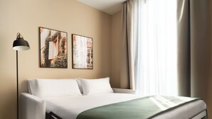 A neatly made bed with a green throw, a floor lamp, and two framed pictures on the wall. - Limehome Alicante Avinguda de Jijona (Alicante)