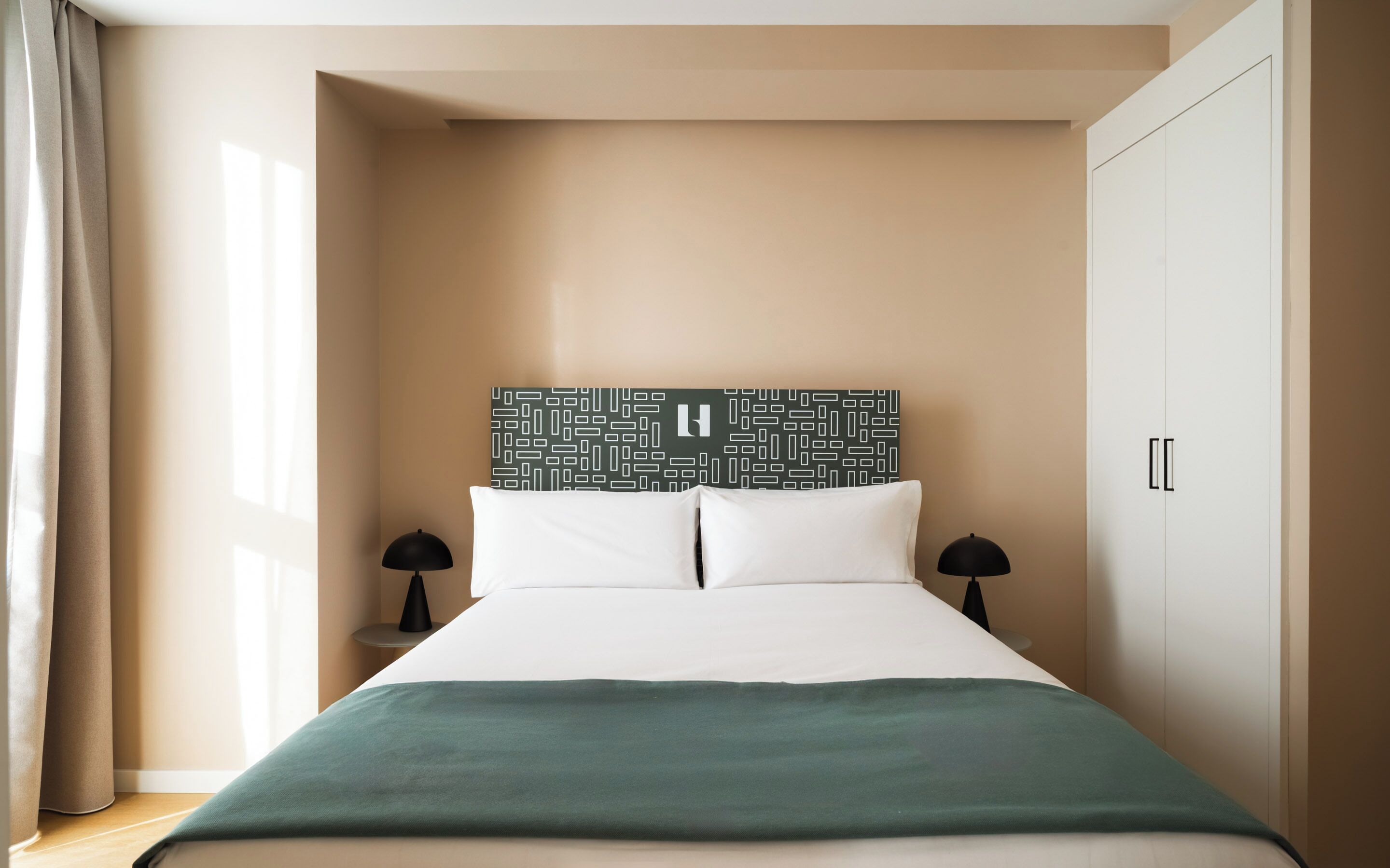 Un dormitorio ordenado con una cama, dos mesitas de noche, un cabecero con diseño geométrico y un armario.