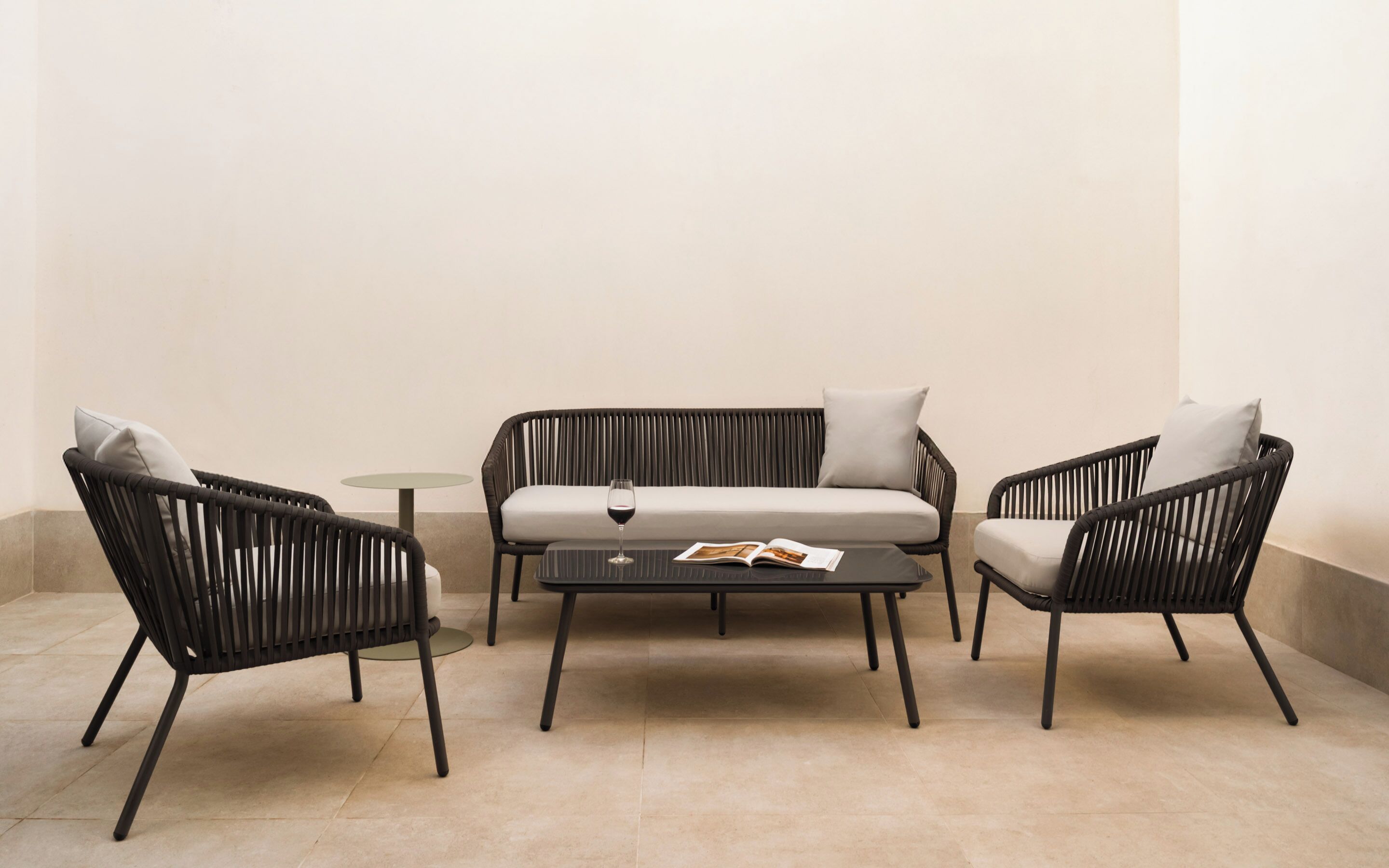 Un espace extérieur moderne, aménagé avec un canapé, deux fauteuils et une petite table ronde.