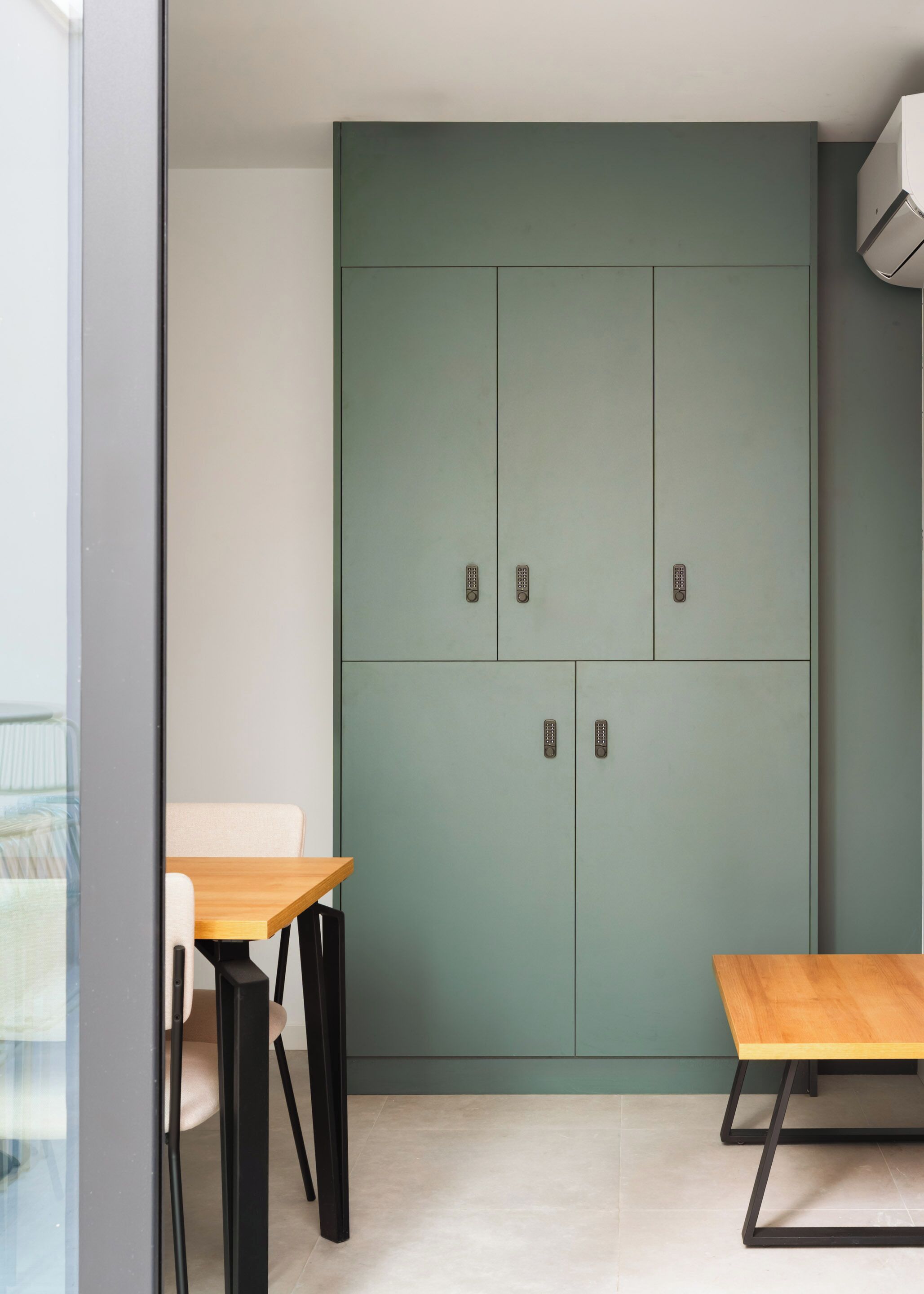 Una habitación con un armario color turquesa, dos mesas de madera y una silla.