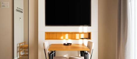 Un'area pranzo moderna con un tavolo e sedie in legno, una TV a schermo piatto montata sopra e uno specchio a parete.
