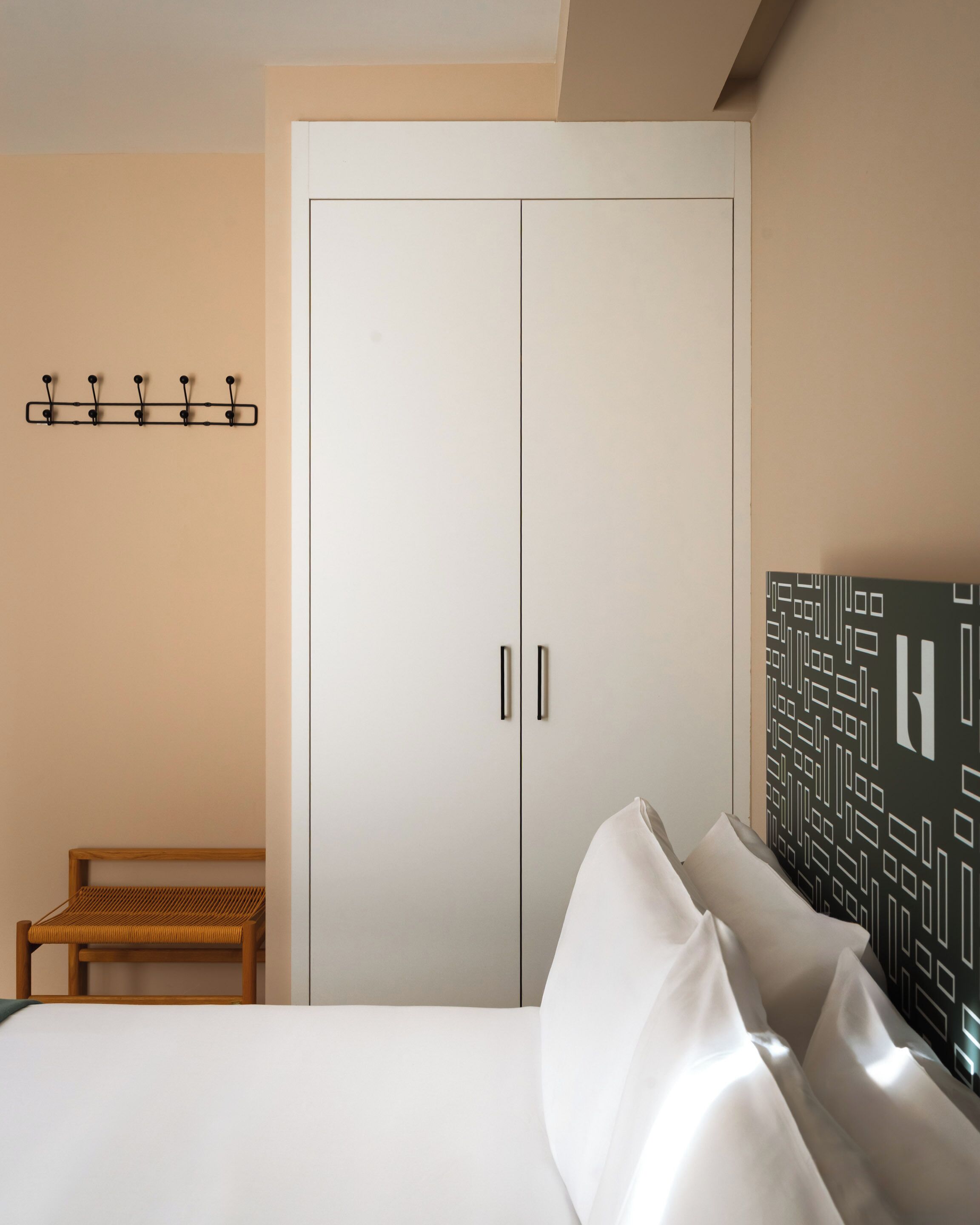 Un dormitorio con cama, banco de madera, armario y perchero de pared.