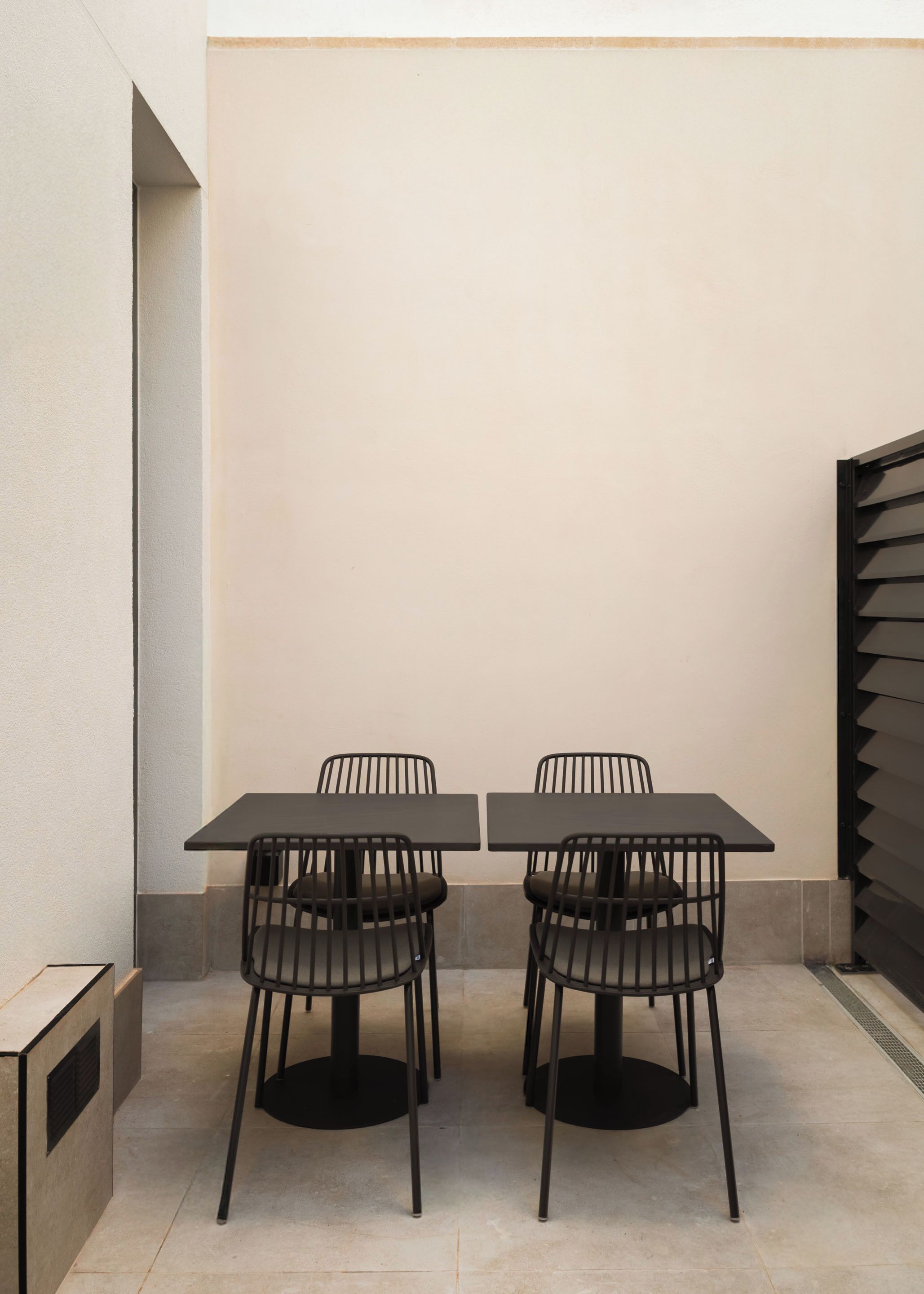 A minimalist outdoor dining area with two square tables and four black chairs.
