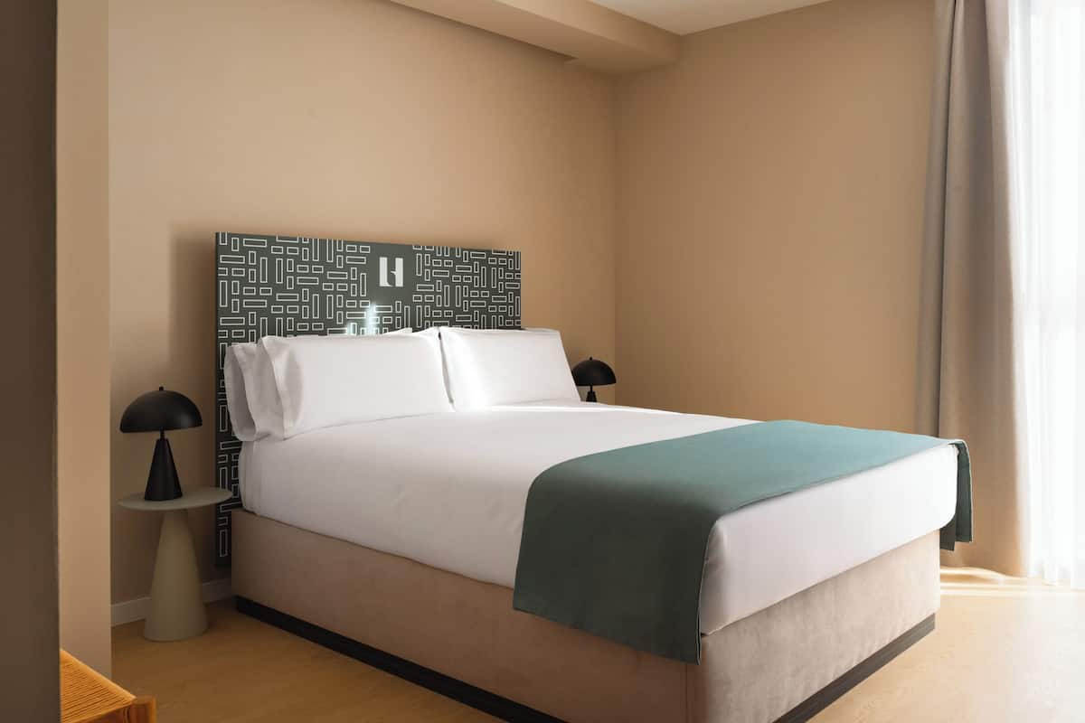 A modern hotel room with a large bed, two bedside tables, and a patterned headboard.