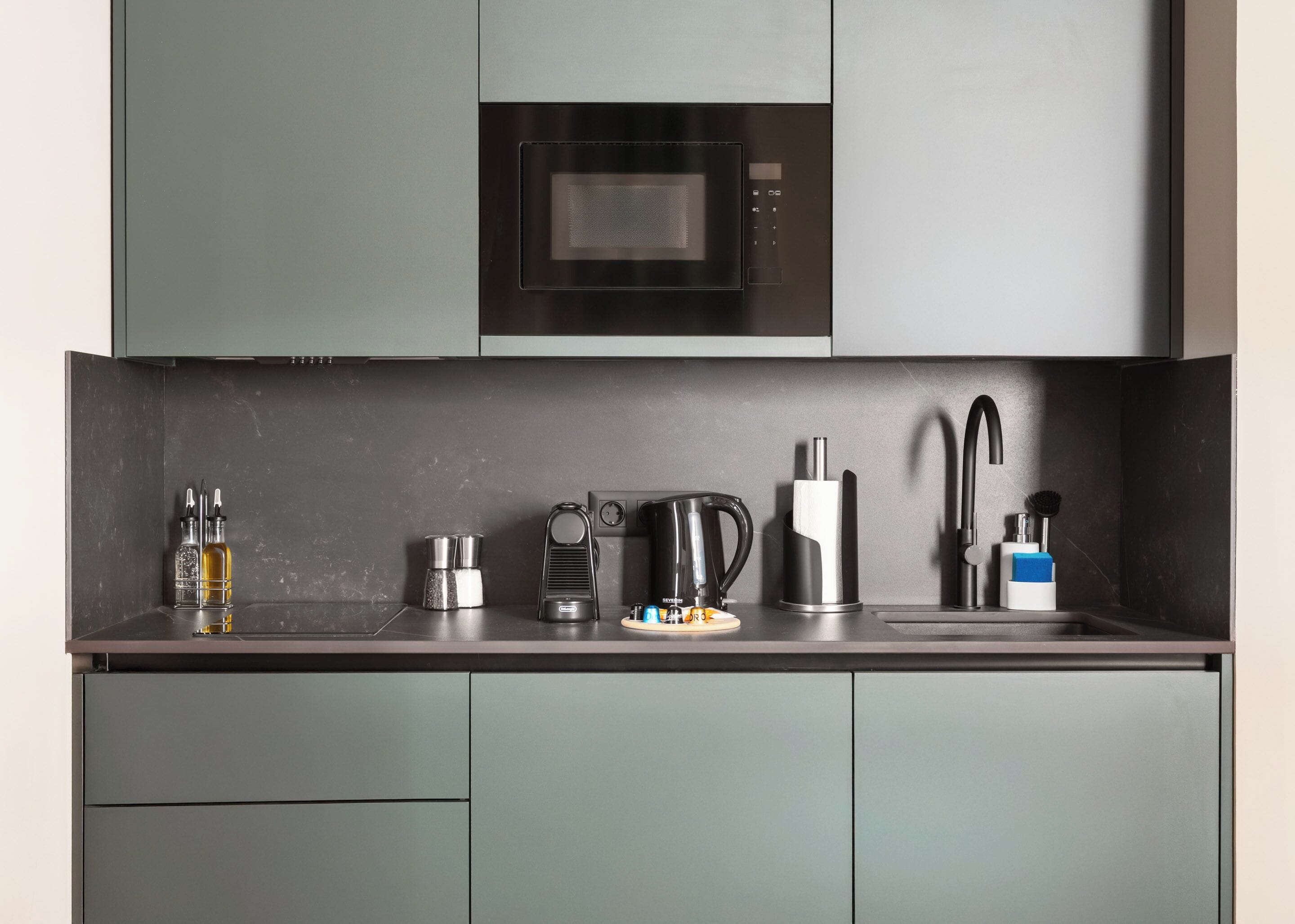 A modern kitchen with a built-in microwave, a kettle, a coffee maker, and a sink with a faucet.