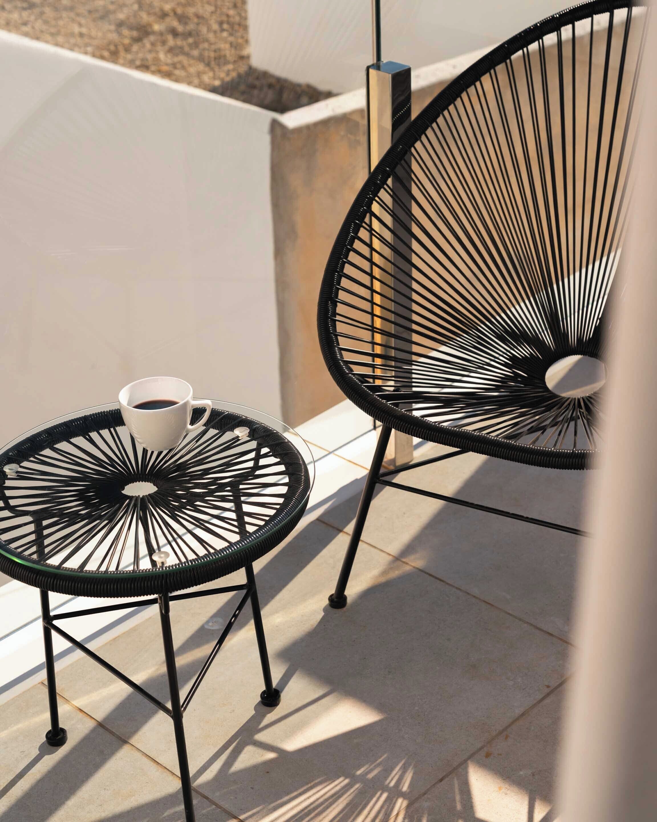 Two black metal chairs with round glass tables on a tiled patio.