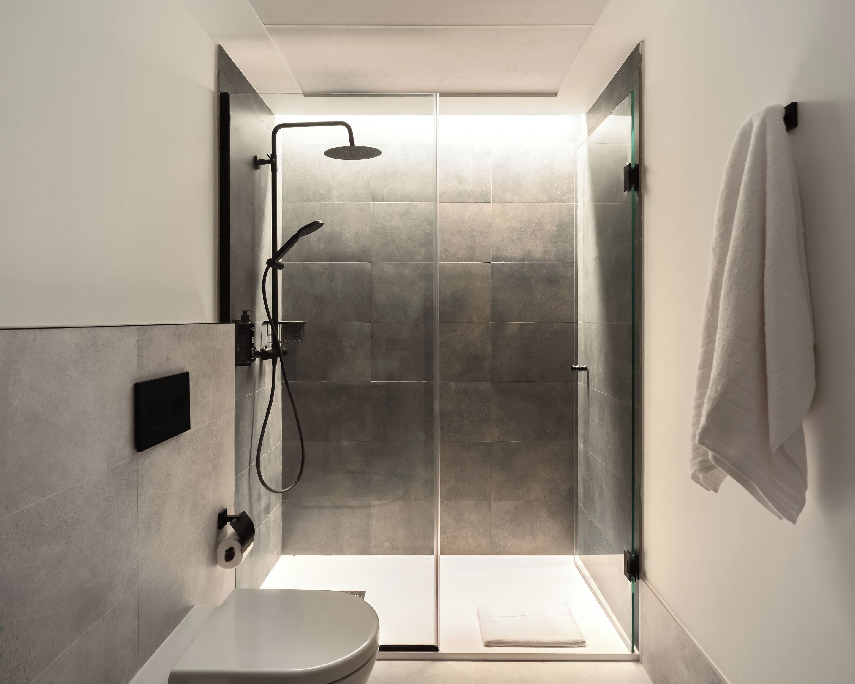 Een moderne badkamer met een douchecabine van glas, een toilet en een handdoek aan de muur.