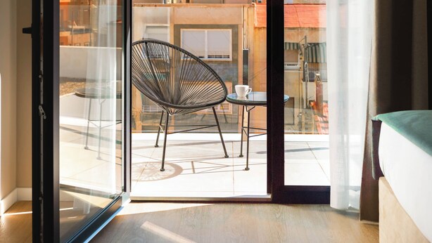 A room with a sliding glass door leading to an outdoor balcony with a chair and table. - Limehome Alicante Avinguda de Jijona (Alicante)