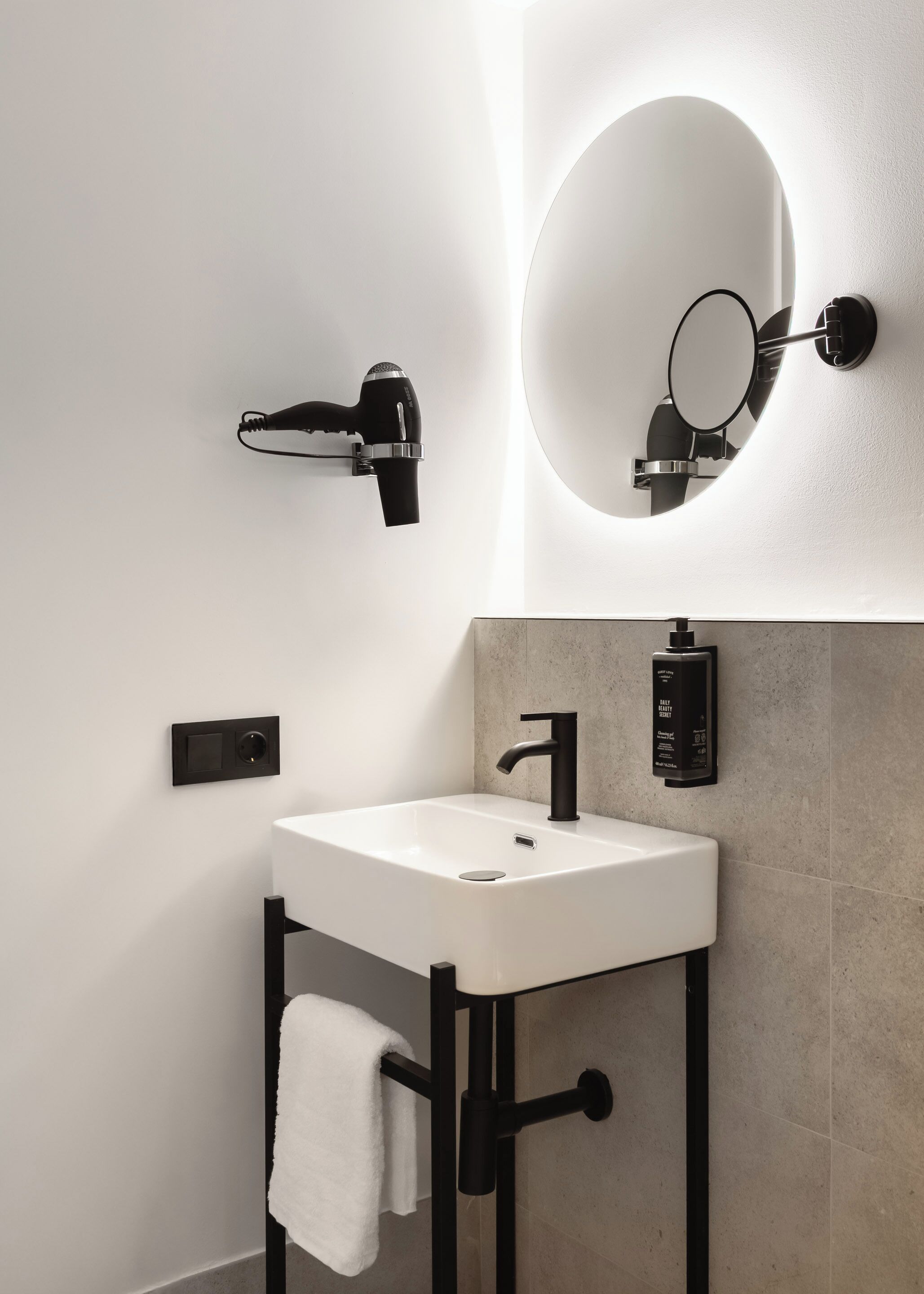 Un bagno moderno con un lavandino bianco, un rubinetto nero e un asciugamano appeso a un porta-asciugamani nero.