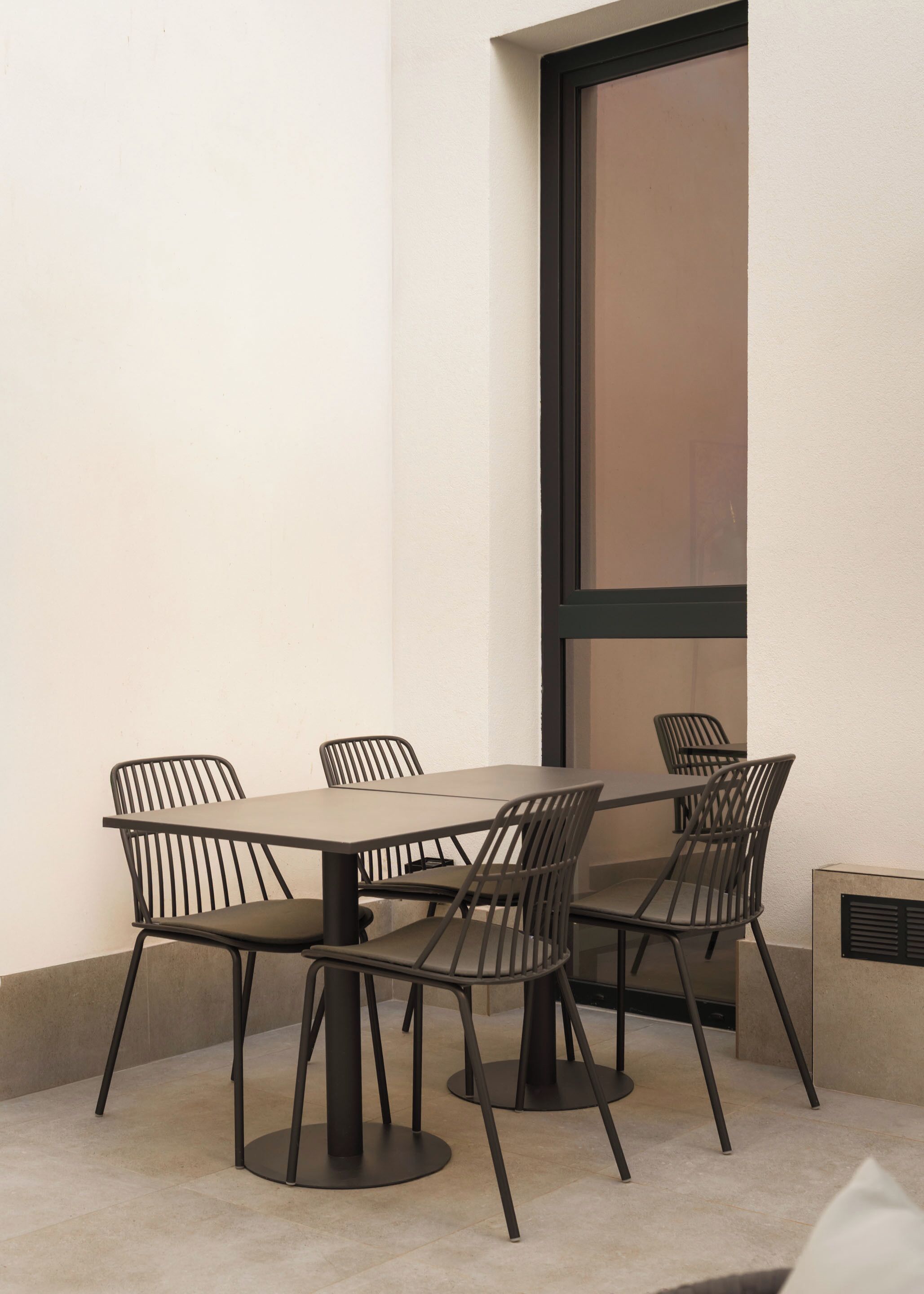 A modern outdoor dining area with a rectangular table and six chairs, featuring a minimalist design and a large window.