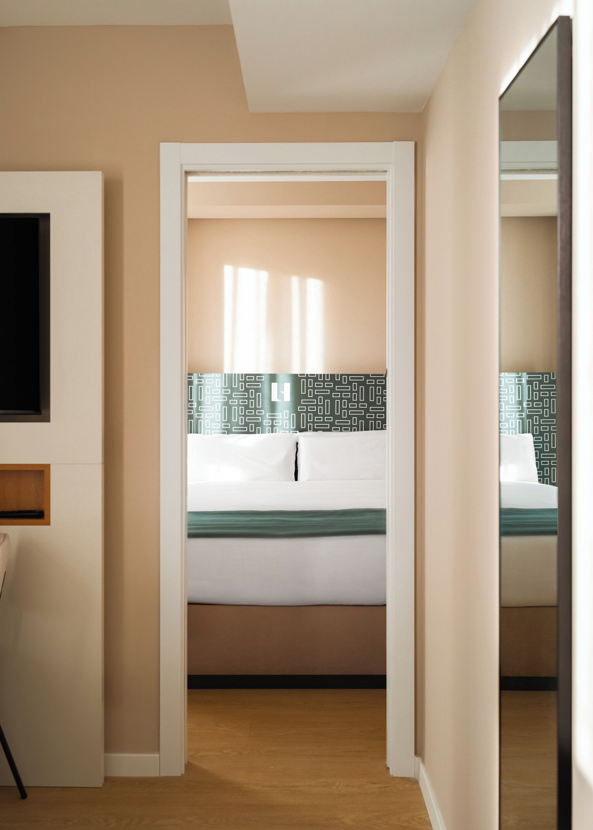 A modern hotel room with a bed, a TV, and a wooden floor.