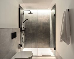 Un baño moderno con cabina de ducha de vidrio, un inodoro y una toalla colgada en la pared.