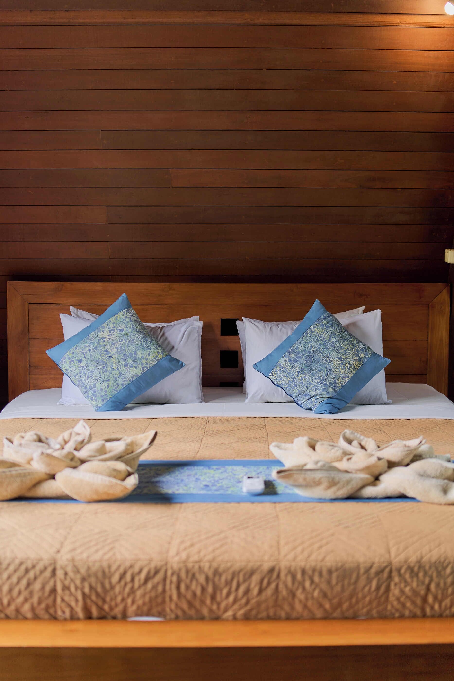 A neatly made bed with two pillows, a wooden headboard, and a wooden floor.