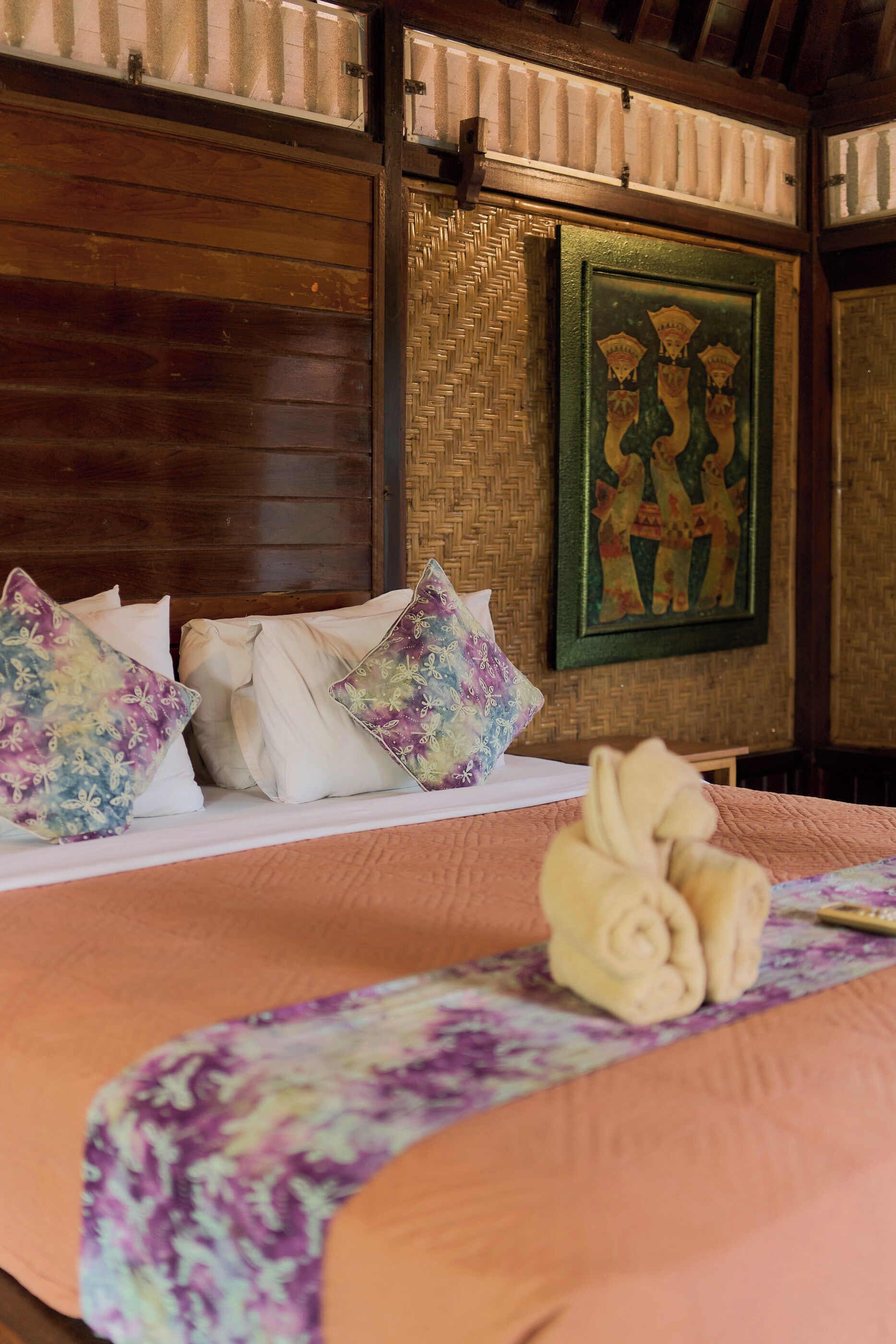 A bed with a floral bedspread, multiple pillows, and a decorative flower arrangement.