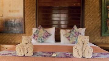 Habitación de hotel con una cama, dos toallas con forma de osos, un control remoto y una colcha estampada con motivos florales.