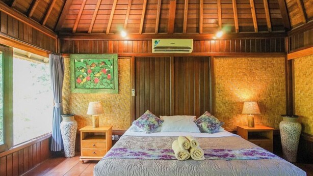 A room with a wooden ceiling, a bed with a patterned bedspread, two bedside tables with lamps, and a woven wall hanging. - ABANGAN BUNGALOW  (Ubud)