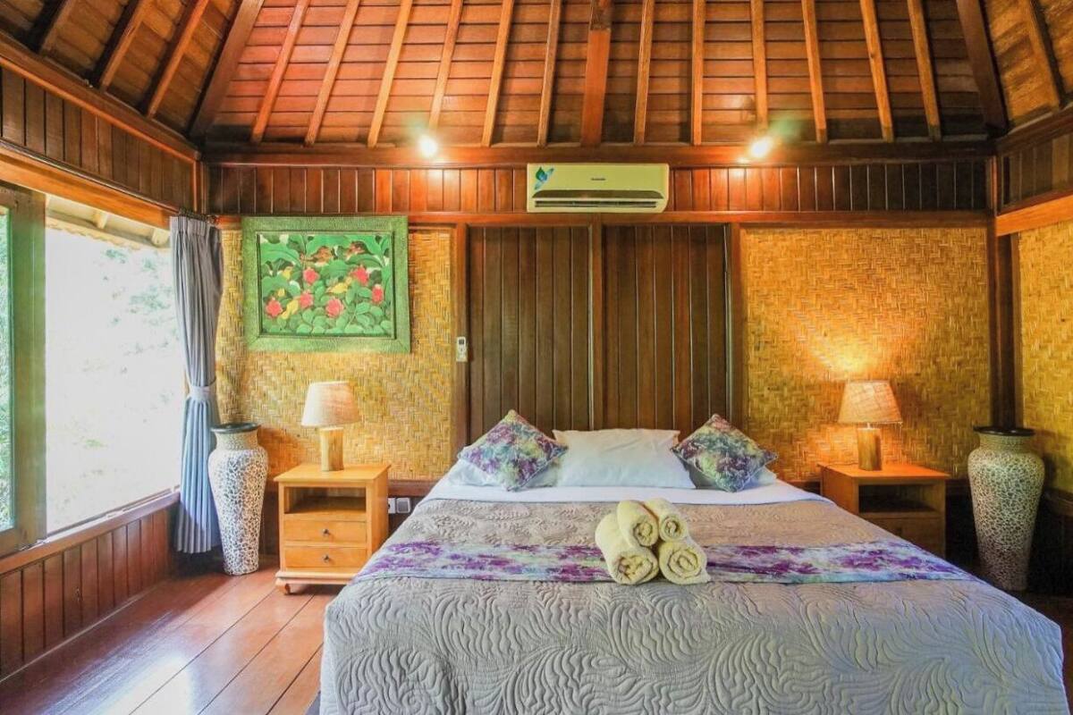 A room with a wooden ceiling, a bed with a patterned bedspread, two bedside tables with lamps, and a woven wall hanging.
