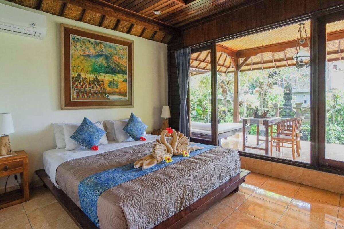 A hotel room with a large bed, a painting on the wall, and a view of the garden through the window.