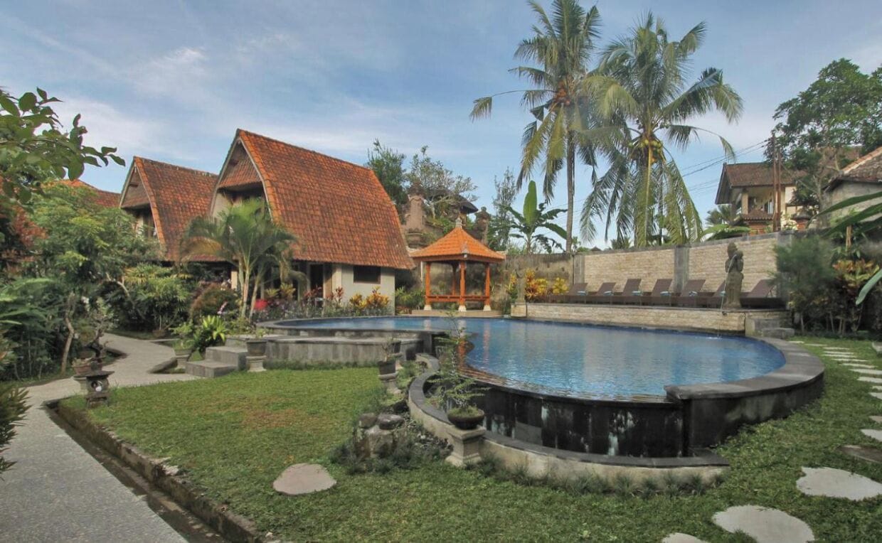 A pool surrounded by a garden with palm trees and a gazebo.