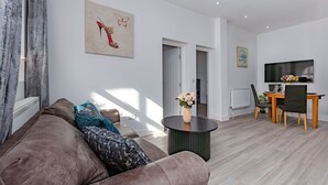 A modern living room with a brown sofa, a round coffee table, and a dining area with a TV and flowers. - Seaside View Retreat in Clacton-on-sea (Clacton-on-Sea)