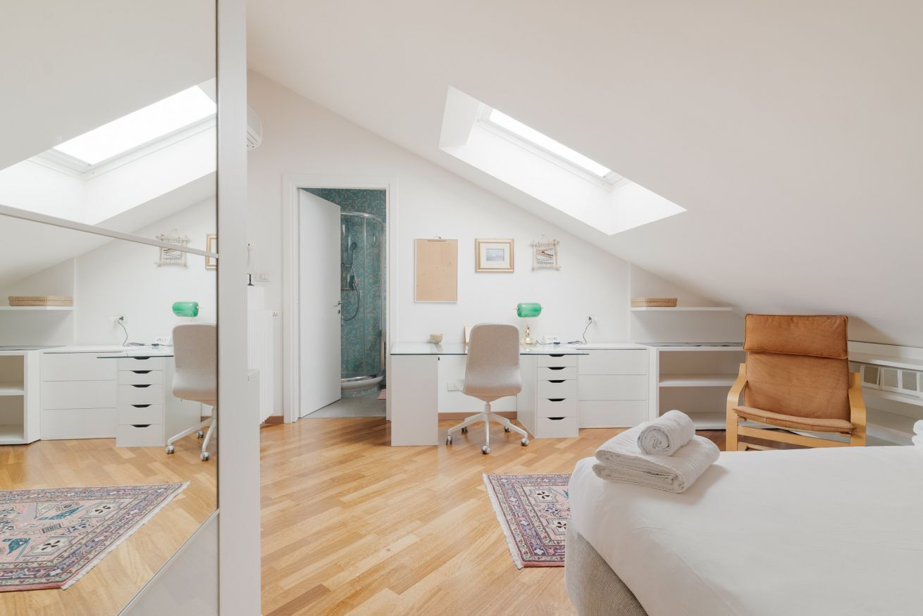 Un dormitorio con tragaluz, escritorio, silla y cama.
