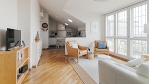 A modern living room with a sofa, armchair, and TV stand. A kitchen is visible in the background. - GuestHost - Elegant and modern 90 square meters apartment, perfect for four people, located on the fifth floor of a building with elevator (NOT suitable for disabled people).The property is located in the Navigli area (limited traffic zone), one of the c (Milan)