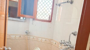 A small bathroom with a toilet, a window, and a shower. - SHRI SHYAM KASHI STAY VARANASI (Varanasi)